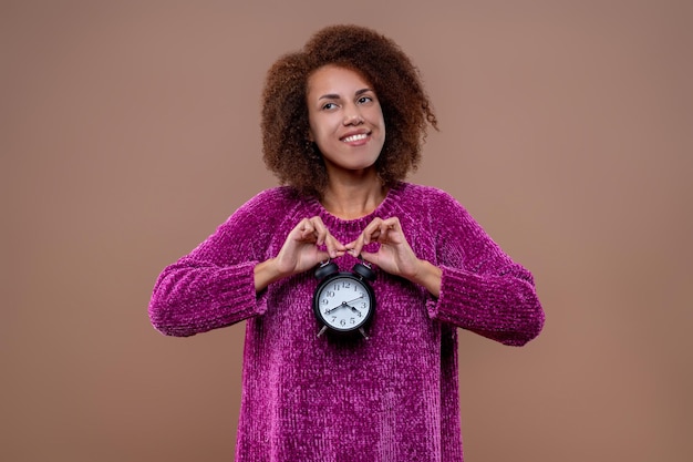 Darkhaired young woman holding an alarmclock in hands