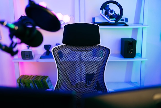 Photo darkroom for a professional gamer with a comfortable empty gamer chair computer table neon lights keyboard monitor controllers and microphone for recording podcasts and live streaming at home