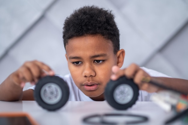 A darkskinned boy playing with toy vehicle wheels