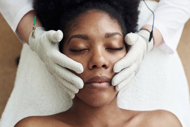 A darkskinned model lies on the couch at the beautician and receives a microcurrent massage