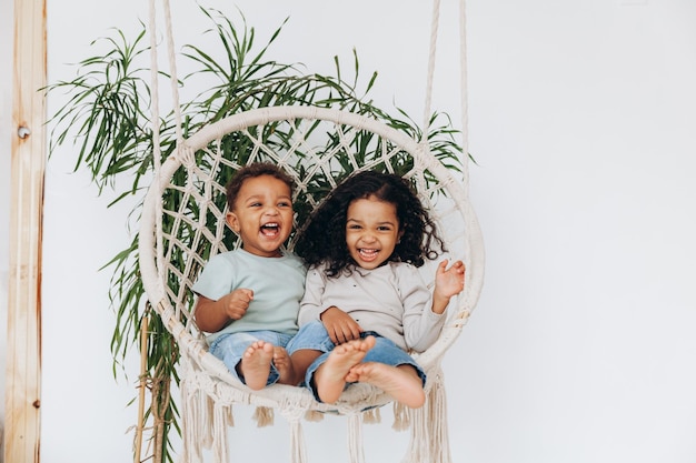 Darkskinned mulattoes A boy and a girl sit in a wicker hanging chair and ride Children love each other and hug