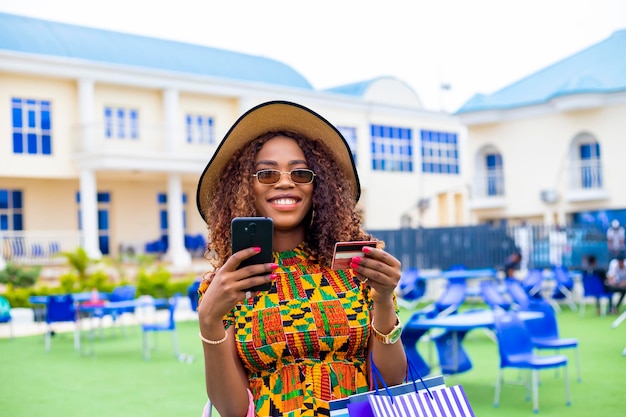 Darkskinned woman satisfied with online shopping holding her bags using mobile phone and credit card