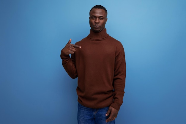 Darkskinned year old guy with a short haircut in a brown sweater laughs on a studio background with