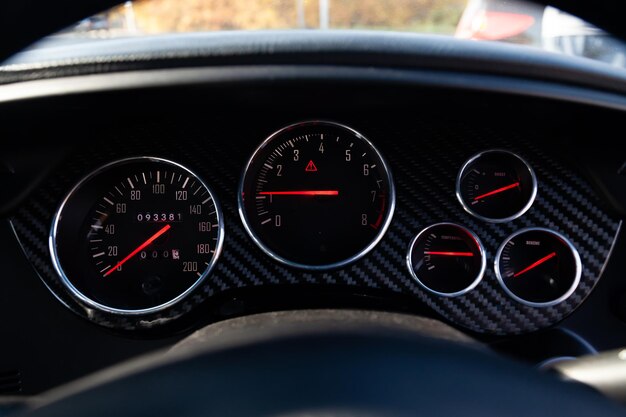 The dashboard of the car with red arrows and carbom trim a speedometer tachometer and other tools to monitor the condition of the vehicle in modern style on black isolated background
