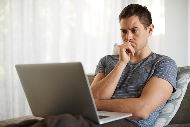 Dat is een denker Shot van een knappe jonge man die zijn laptop thuis gebruikt