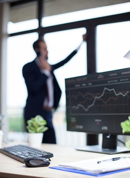 Data analysis displayed on marketing specialist computer in his office. Young entrepreneur in the background.