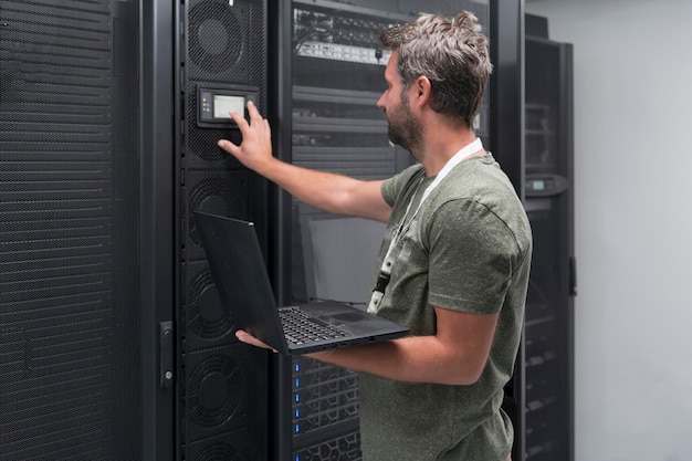 Data Center Engineer Using Laptop Computer. Server Room Specialist Facility with Male System Administrator Working with Data Protection Network for Cyber Security or Cryptocurrency Mining Farm.