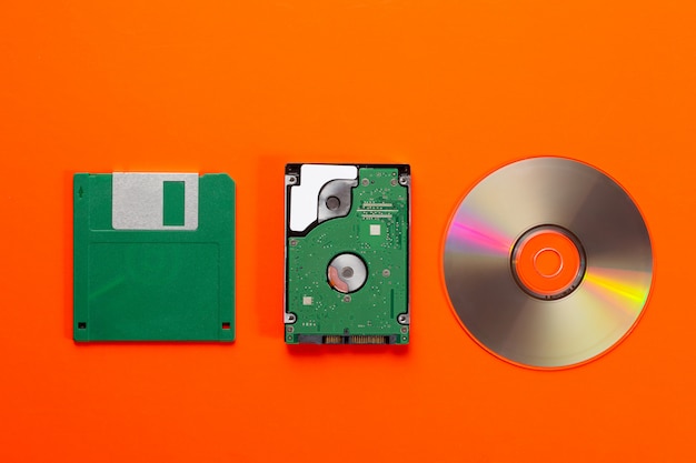 사진 데이터 저장 매체 진화-플로피 디스크, cd 디스크, 주황색 배경에 작은 하드 디스크 드라이브.