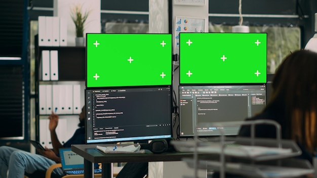 Database developer analyzing greenscreen display on multiple screens, working with server code on monitors. System engineer using isolated copyspace chromakey with mockup template in office.