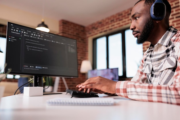 Database-ontwikkelaar met programmeeralgoritme voor draadloze hoofdtelefoons met behulp van een personal computer die op afstand werkt in de woonkamer. Afro-Amerikaanse freelance coder die thuis code schrijft en debugt.