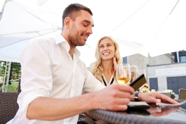 date, people, payment and finances concept - happy couple with credit card and wine glasses paying bill at restaurant