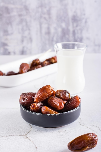 Dates in a bowl and a glass of milk on the table Food for the holy month of Ramadan Vertical view