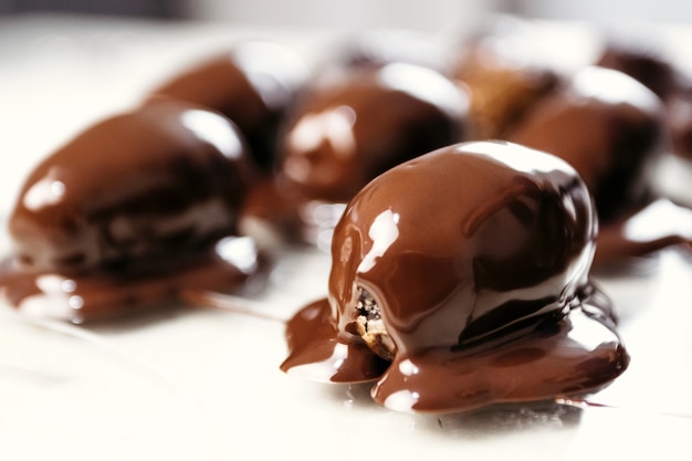 Dates in chocolate, dessert. Confectioner pours chocolate over dessert. Macro, close-up.