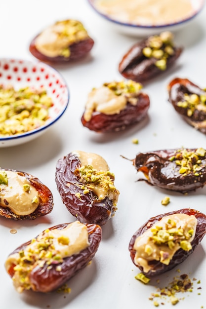 Dates stuffed with peanut butter, chocolate and pistachios on white background.