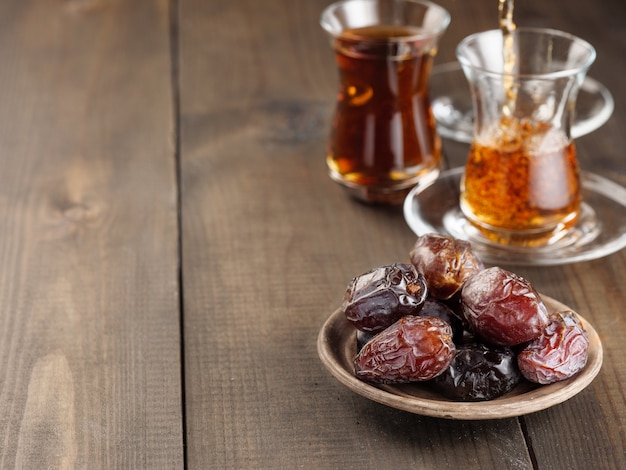 Dates with black tea on a wooden table. Traditional iftar food during Ramadan.