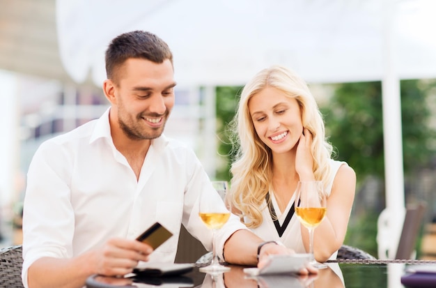 datum, mensen, betaling en relaties concept - gelukkig stel met creditcard, rekening en wijnglazen op het terras van het restaurant
