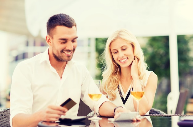 datum, mensen, betaling en relaties concept - gelukkig stel met creditcard, rekening en wijnglazen op het terras van het restaurant