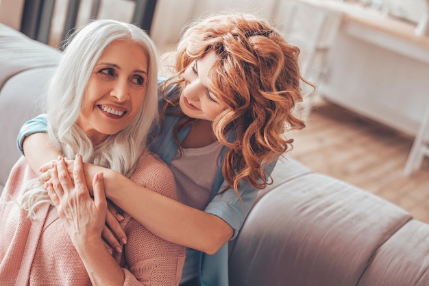 Photo daugher hugging mother sitting on the sofa at home