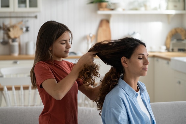 Daughter braiding mothers long wavy hair mom and child enjoying time with each other at home