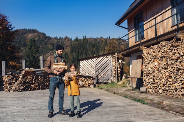 Дочь и папа осенью держат наколотые дрова во дворе.