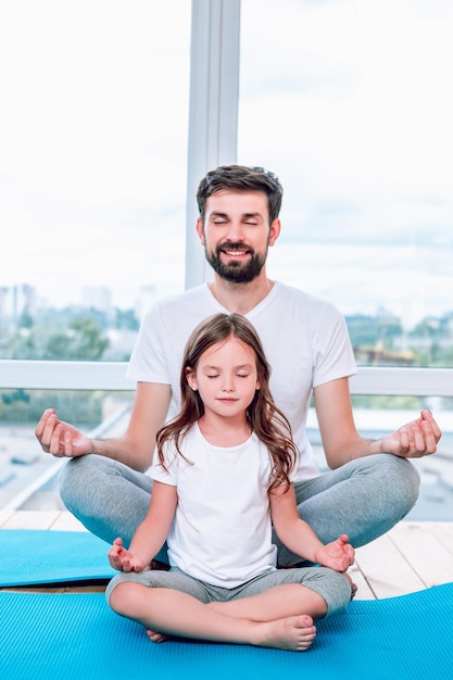 Daughter and dad meditating with closed eyes together sitting in lotus position