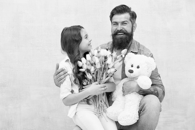 娘と父は誕生日の女の子を祝う父の日とお父さんに挨拶テディベアと幸せな家族の肖像春の花の花束女性の日母の日のためにチューリップを準備する