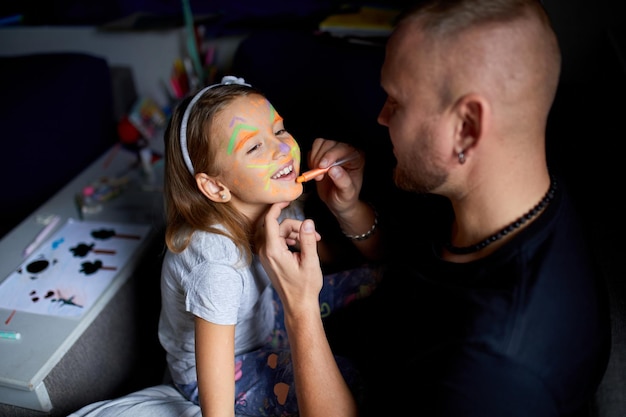 Daughter and father paint a face having fun leisure together at home