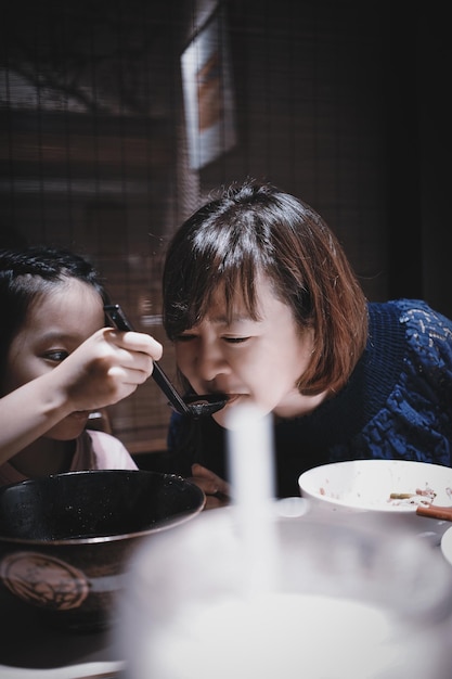 사진 레스토랑 에 앉아 있는 딸 이 어머니 에게 음식 을 먹이고 있다