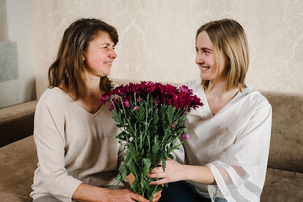 The daughter gives flowers to her mother and congratulated mother's day Portrait mother and grandmother smiling and spend time together at home International Women's Day Happy holiday concept