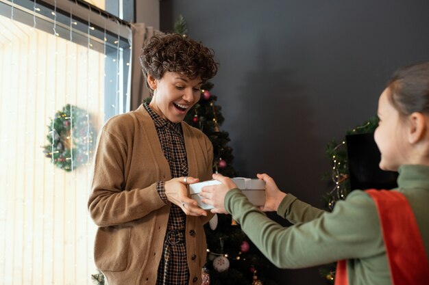 家で光と飾られた木に対して興奮した母親にクリスマスプレゼントを与える娘