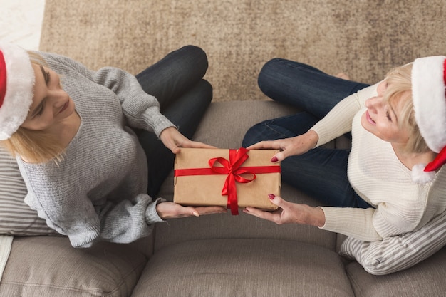 Daughter giving a gift to adult mother. Spending time together, celebrating a holiday at home on weekend. Generation, relationship, celebration, present, New Year, Christmas concept, top view