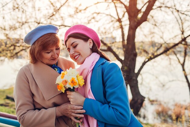 Daughter giving her senior mother bouquet of flowers by spring river