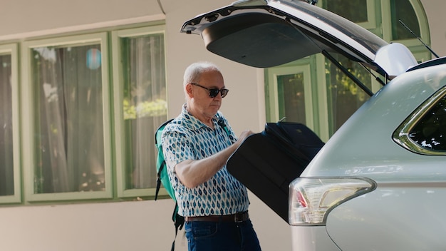 Daughter and grandparents loading voyage luggage inside car trunk while going on summer field trip. People putting baggage and trolleys inside vehicle while getting ready for citybreak departure.