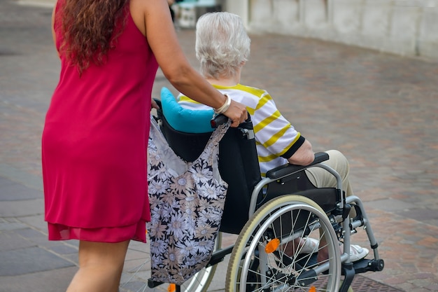 Daughter helps her elderly disabled mother in a wheelchair