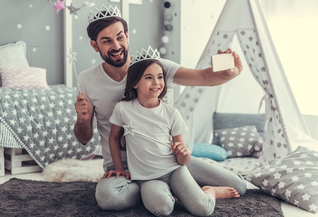 Daughter and her young dad in crowns are doing selfie.