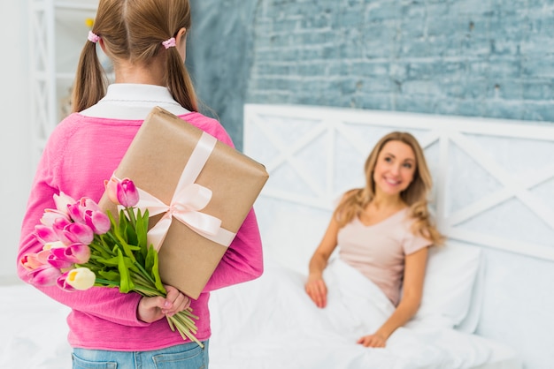 Photo daughter holding gift and tulips for mother in bed