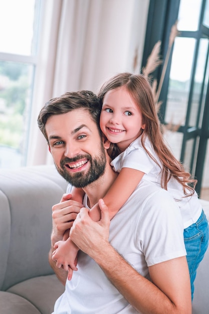 Daughter hugging handsome father sitting on the sofa at home