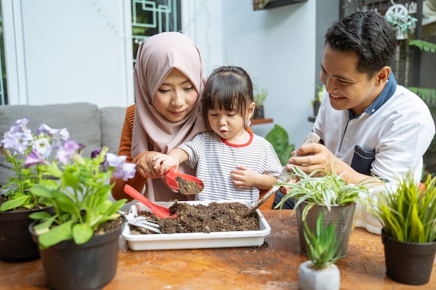 Daughter is assisted by her mother by holding a small shovel to take ground and her father holding a small shovel