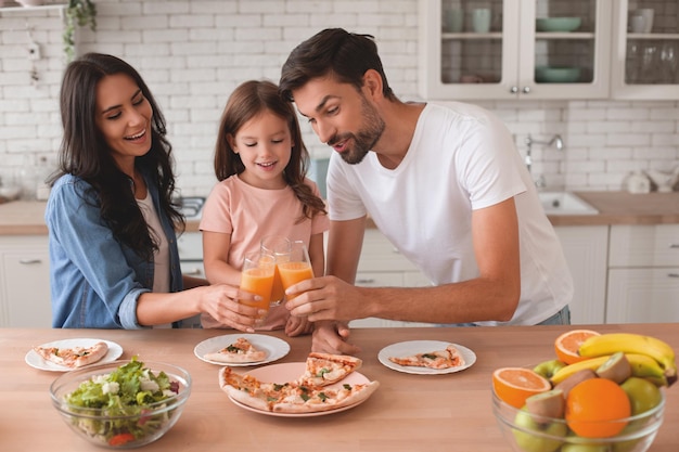 Daughter mother and father clicking glasses with orange juice together standing at kitchen table