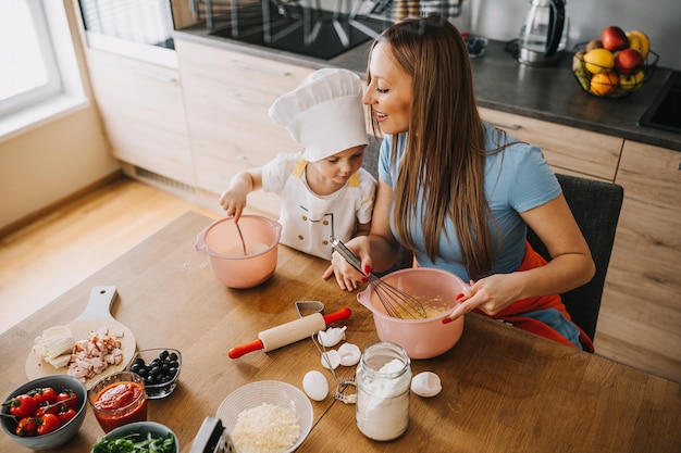 Daughter and mother making pizza together for dinner at the kitchen preparing dough