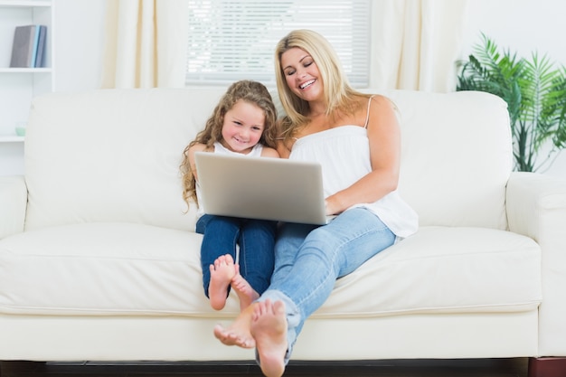 Дочь и мать, отдыхая на диване с ноутбуком