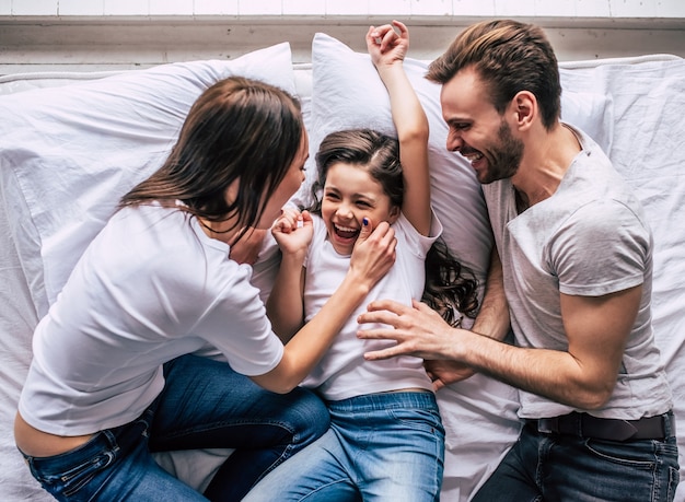 The daughter and parents joying on the bed