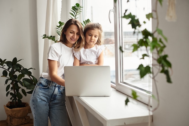 Daughter plays with mom and cat while mom works on computer