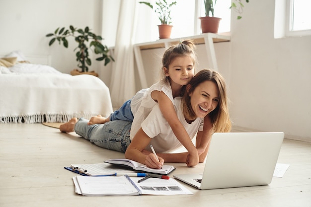 Daughter plays with mom and cat while mom works on computer