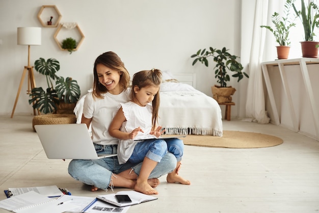 Daughter plays with mom and cat while mom works on computer