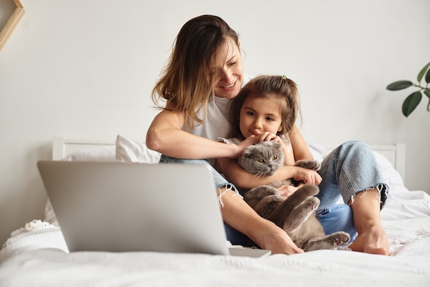 Daughter plays with mom and cat while mom works on computer