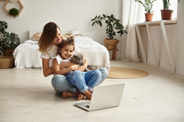 딸이 엄마와 고양이와 함께 재생하는 동안 엄마는 컴퓨터에서 작동합니다.