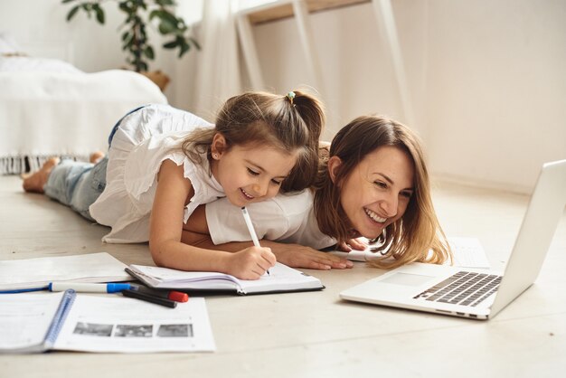 Daughter plays with mom and cat while mom works on computer