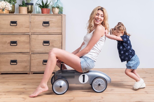 daughter pushes mother sitting on toy racing car