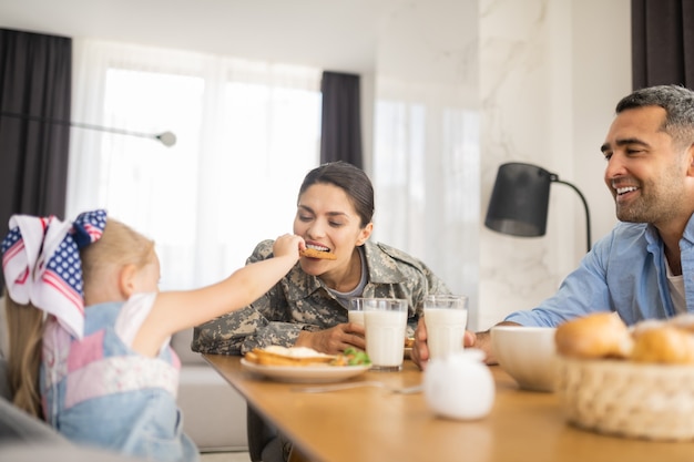 Daughter sharing cookie. Lovely daughter sharing her cookie with mother while having family breakfast